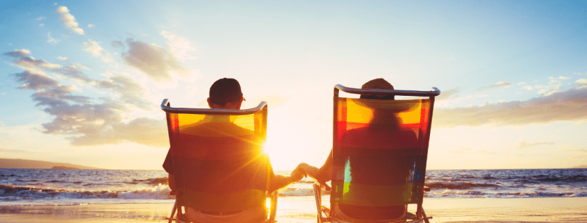 retired couple sitting on the beach in lounge chairs together watching the sunset