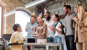 happy employees wearing party hats singing happy birthday to a coworker