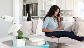 Professional woman working at home on the couch on a laptop and talking on the phone.