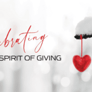 SpiritofGiving_2025_blog Celebrating the Spirit of Giving on a snowy background with a red heart ornament hanging from a tree branch