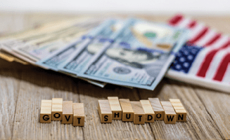 govt shutdown spelled with blocks with money spread on Aemerican flag on a table