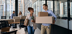Corporate worker holding potted plant and file folders and looking at coworker with cardboard boxes as business relocates